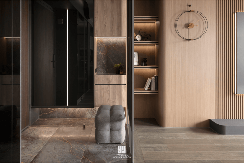 泰御天鑄室內設計：台中新成屋玄關落塵區，以深色紋理石材地坪銜接溫潤木質格柵牆，結合圓弧曲面收納櫃、穿鞋椅與隱藏式燈帶，形塑現代極簡空間層次感。