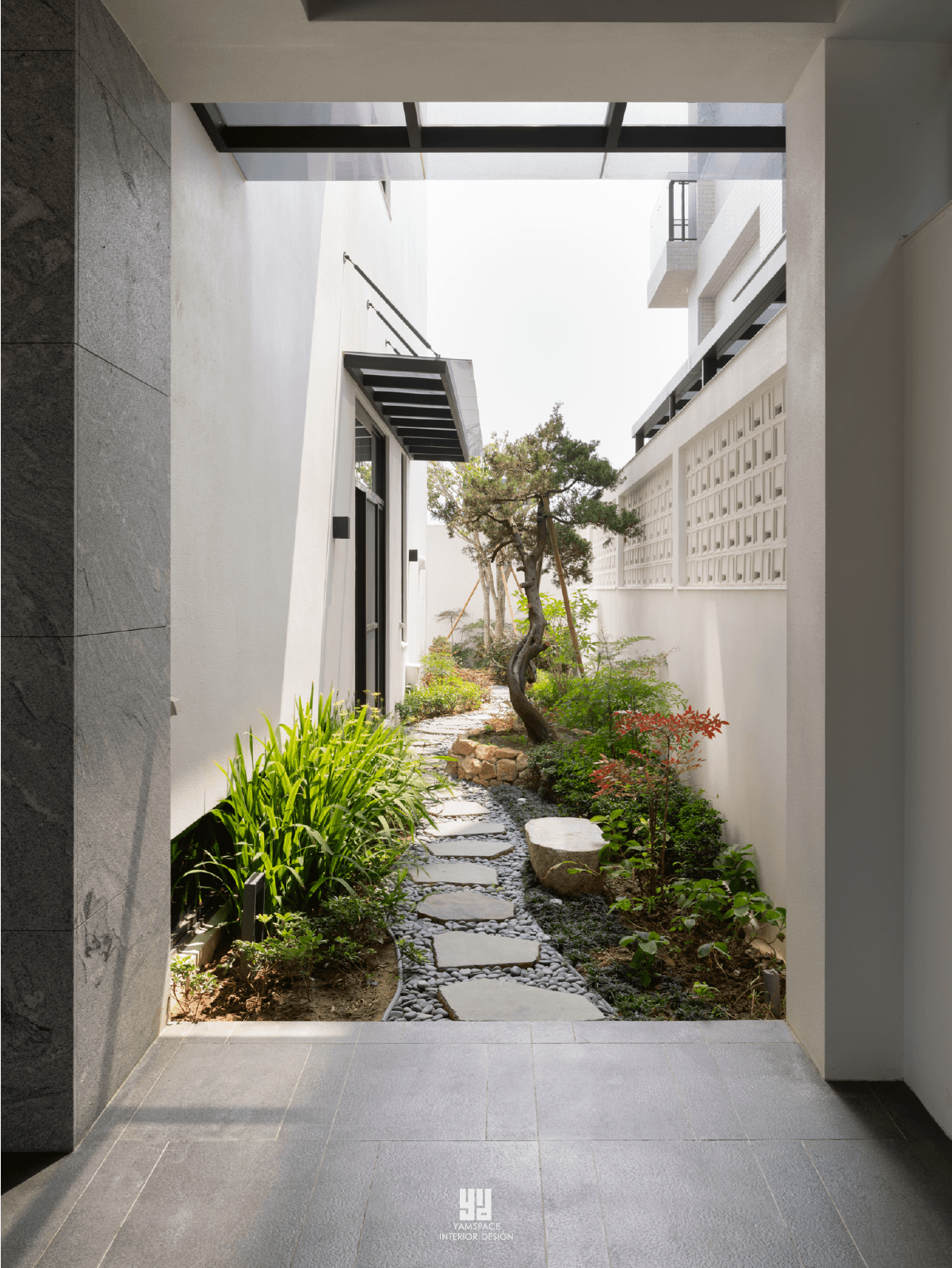 台中北屯自地自建電梯別墅戶外側院：石板小徑串聯松樹景觀，搭配白色花格牆與灰色大理石量體，引入自然氣息進入室內動線。