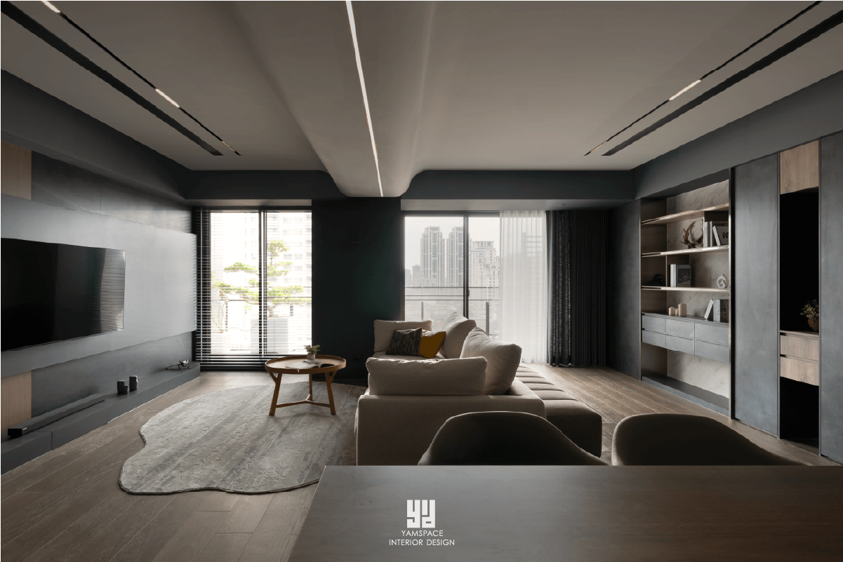 泰御天鑄台中新成屋客廳設計：採用深灰色大器電視牆搭配大面落地窗，利用造型弧形天花板修飾樑柱並嵌入線性燈帶，結合暗色系軟裝與現代極簡家具，營造沉穩且具透視感的公領域空間