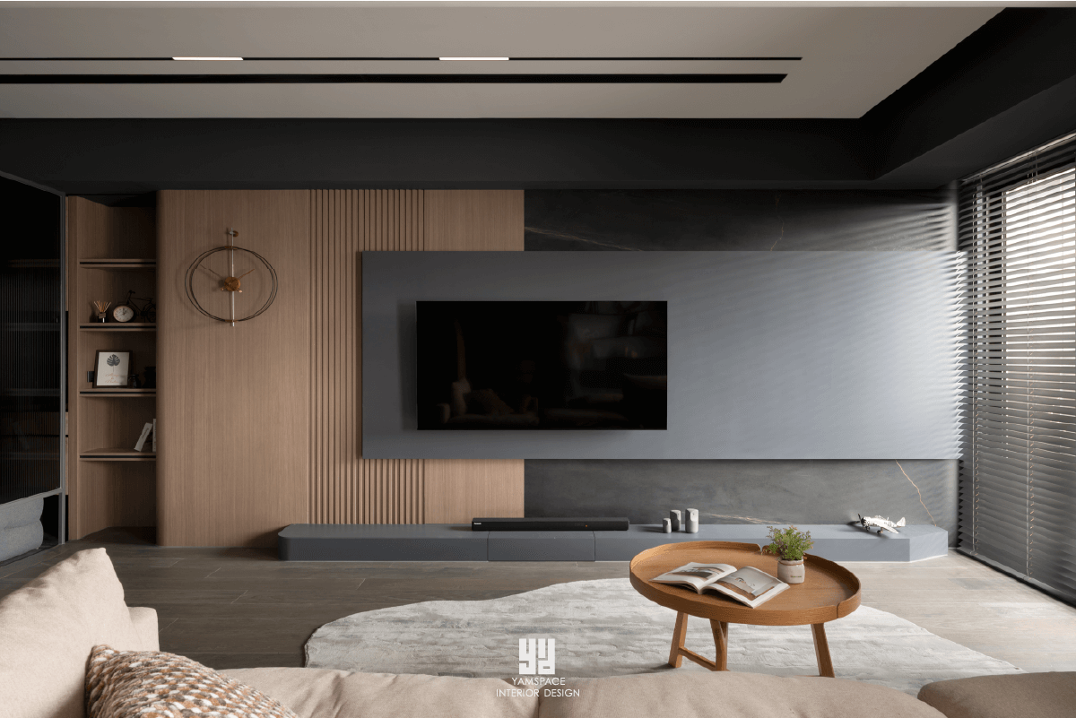 泰御天鑄台中新成屋電視牆設計：以懸浮式深灰面板結合溫潤木質格柵，背景點綴大理石紋板材，搭配嵌入式開放層架與現代簡約掛鐘，透過異材質拼接展現極簡客廳的視覺層次。