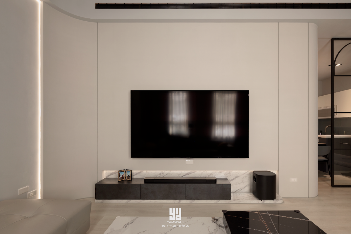 神岡透天舊屋翻新｜現代仛寂風：1F 客廳橫向電視牆採大理石檯面矮櫃、懸浮金屬層板與隱藏式線型燈帶，兩側以大角度圓弧白牆收口，呈現極簡乾淨的電視主牆設計。